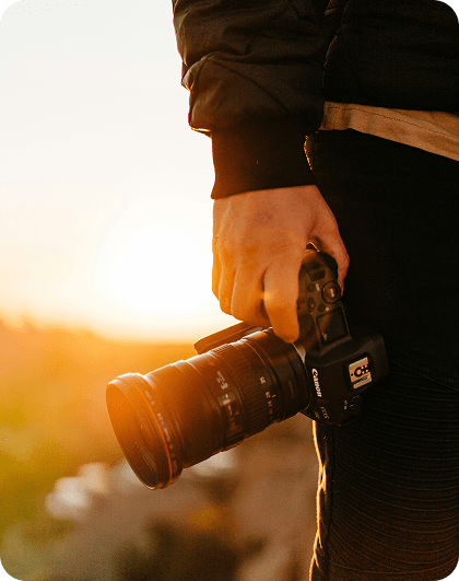 A person holding a photo camera at their side with a sunny sky in the background