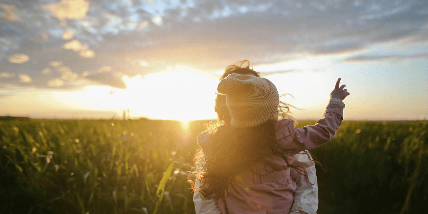Woman holding a child in a field with a sunset